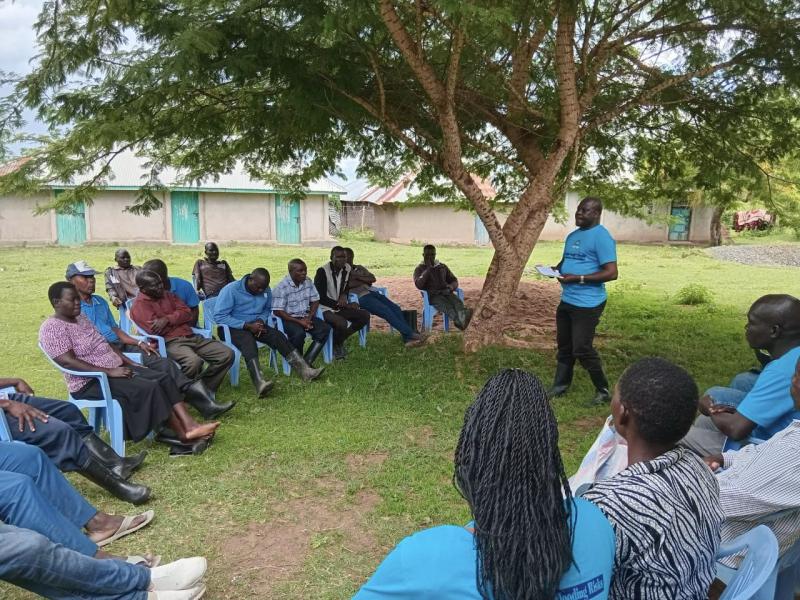 Group of people sitting outside in a circle listening to a speaker