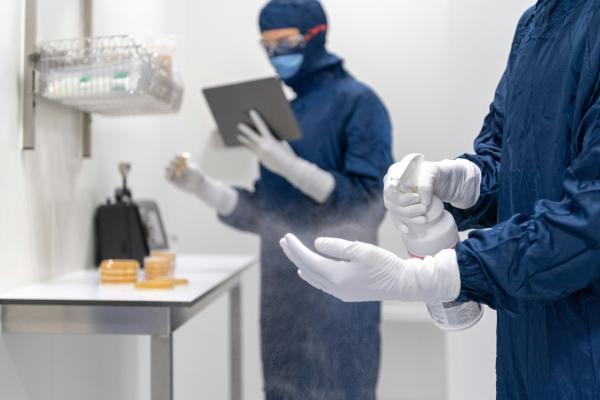 Medical facilty. Two people are in blue PPE with white gloves and one of them is spraying their hand.
